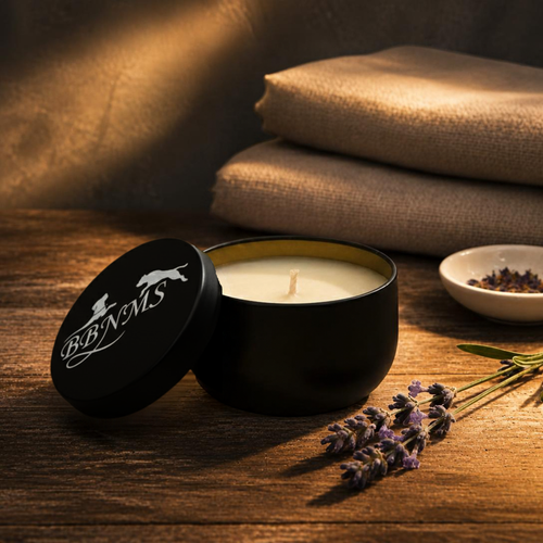 Black candle tin on wooden surface. Lavender is resting next to it with folded tablecloths in the background.